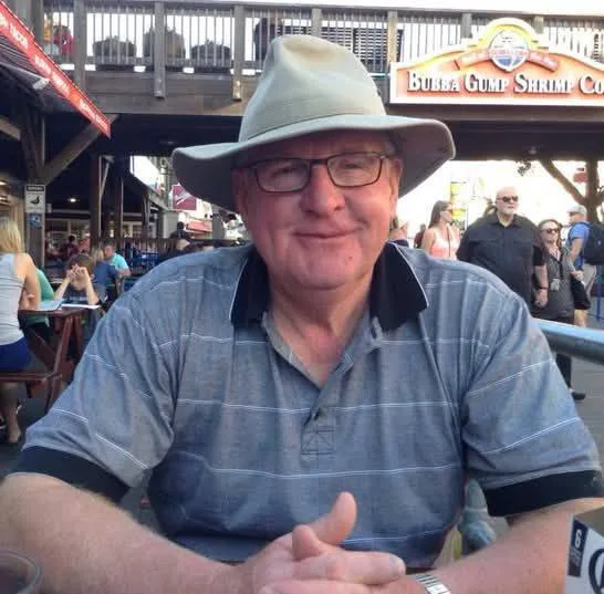 Man in hat and glasses sitting near Bubba Gump Shrimp Co. restaurant.