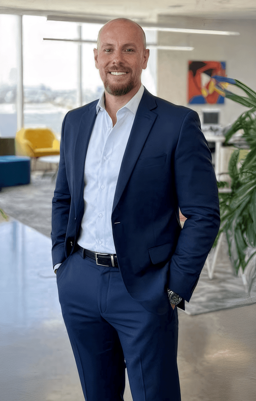 A smiling man in a blue suit and white shirt stands in a modern, bright office adorned with colorful furniture, artwork, and decor—showcasing the results of high-end painting services Florida.