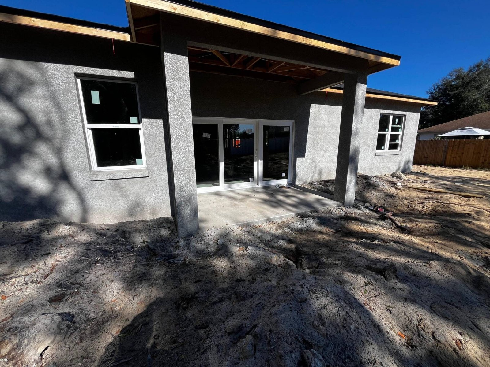 New home construction with stucco exterior, white framed windows, and patio with sliding glass doors.