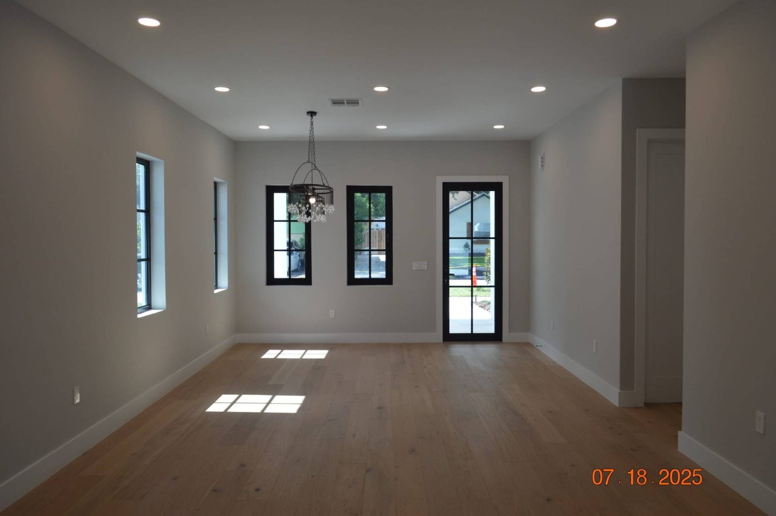 Bright, modern living room with hardwood floors, black windows, and chandelier.